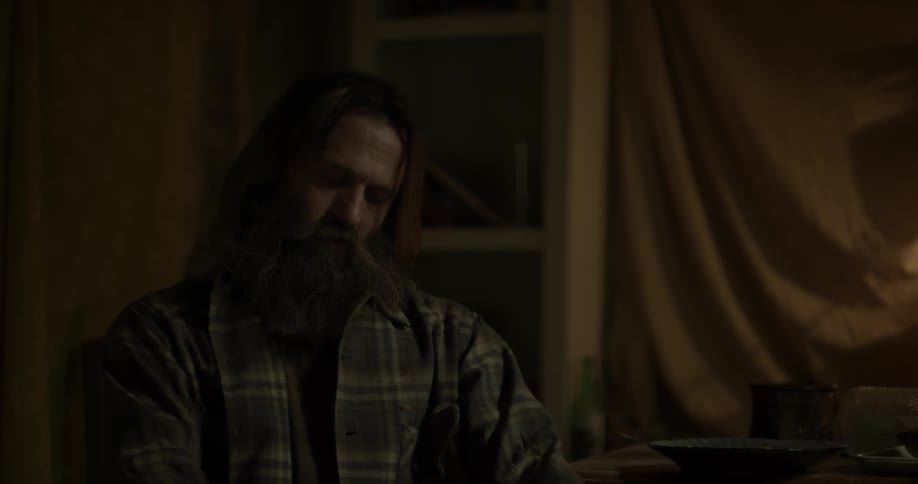 A man with long hair and a long beard is sitting around in a tent