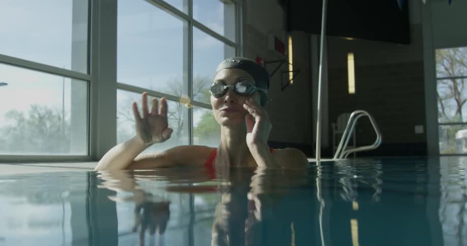 Woman puts on swim goggles in a pool then begins to swim