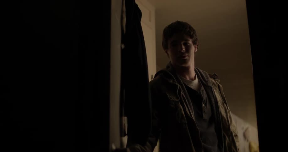 A teenage boy is opening a bedroom door and looking in