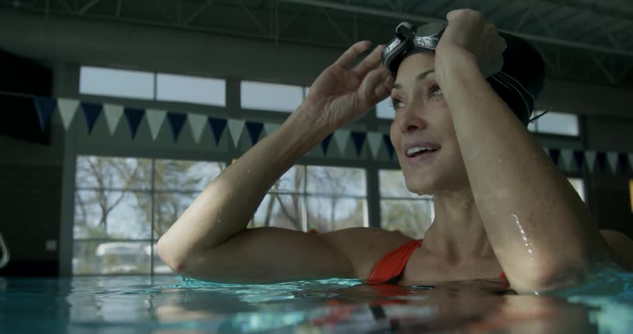 A woman takes off swim goggles and smiles