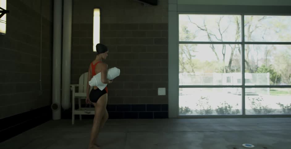 A swimmer walks beside a pool smiling