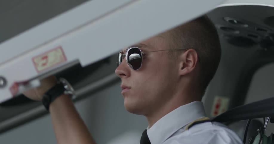 A man wearing sunglasses is strapping into the cockpit of a plane