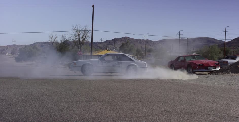 A man spins his car in circles on a rural street on a sunny day