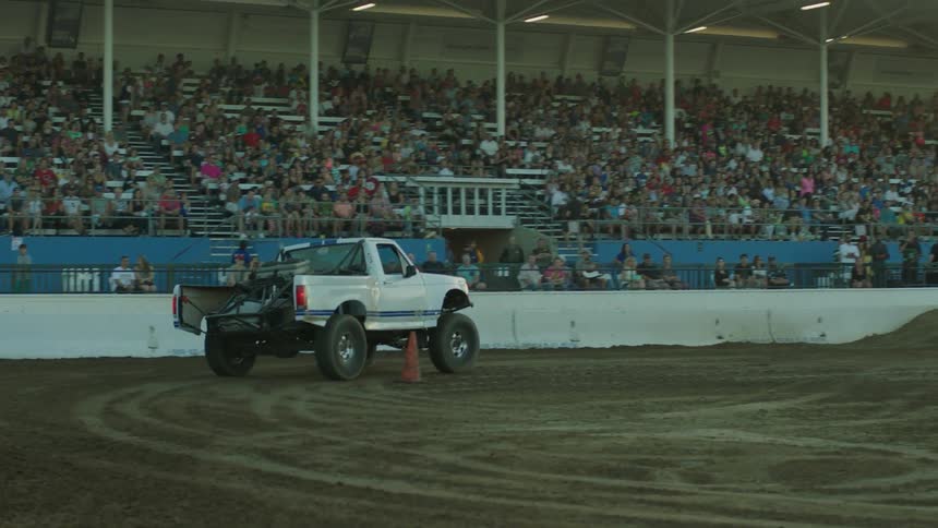 A couple of trucks are racing around a dirt track and over small jumps