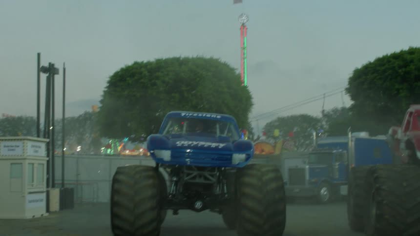 Large monster trucks are being filmed driving towards the camera