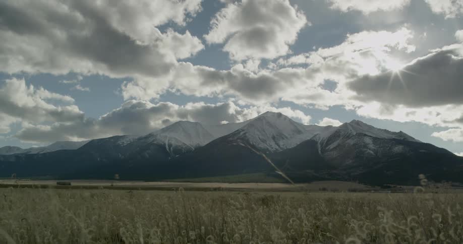 A field with a snow covered mountain rage up ahead on a cloudy day
