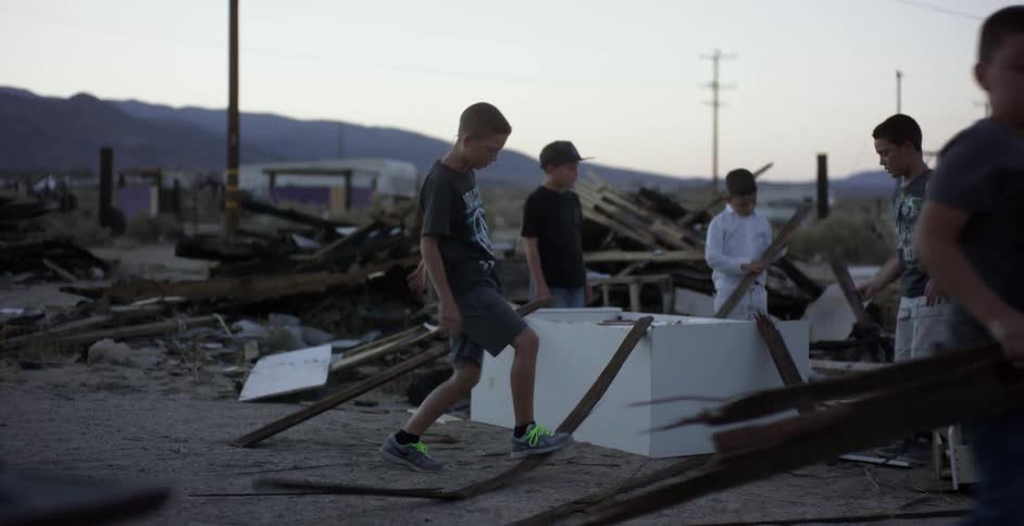 A group of young kids are breaking boards in a pile of rubble