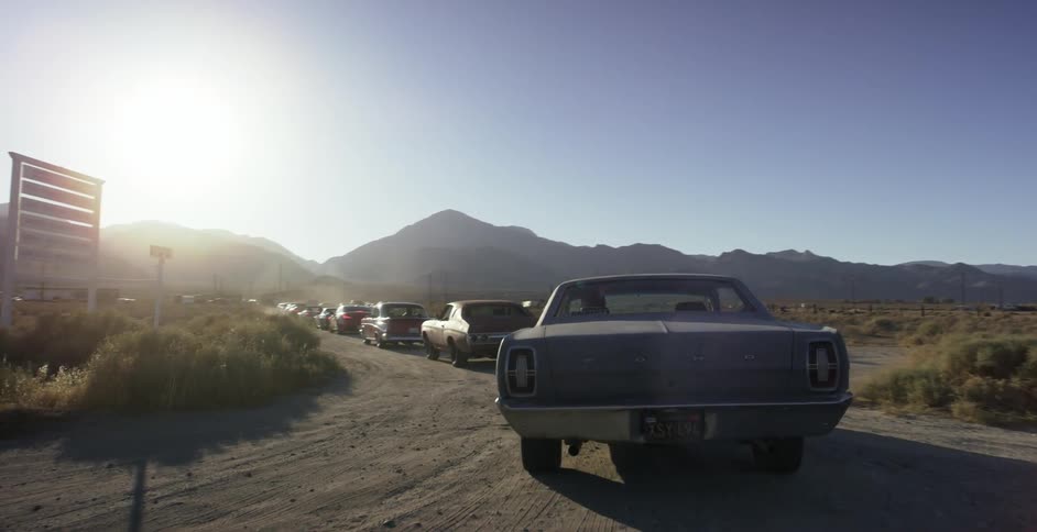 A bunch of classic cars are pulling onto a dirt road in the desert