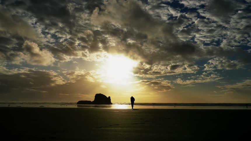 Person walks on a beach at sunset