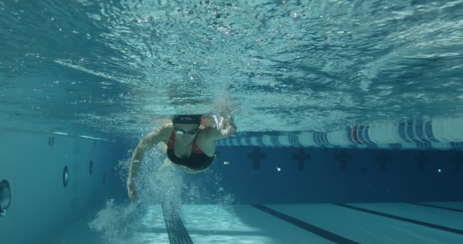 A woman is swimming towards the camera in a large pool
