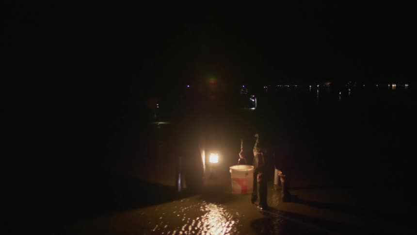 Two man are on the beach at night gathering up clams
