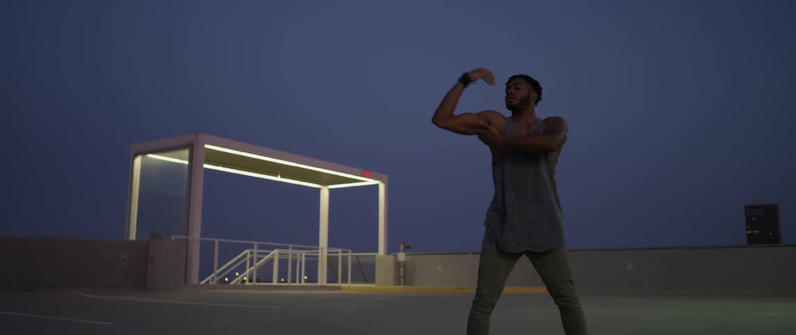 A man dances on the top level of a parking garage at night
