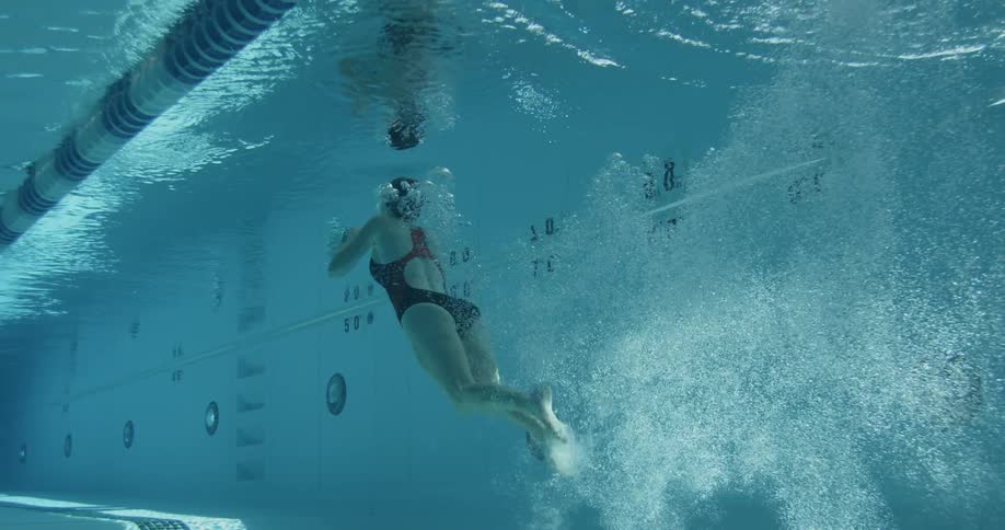 A woman dives into a pool and swims during the day