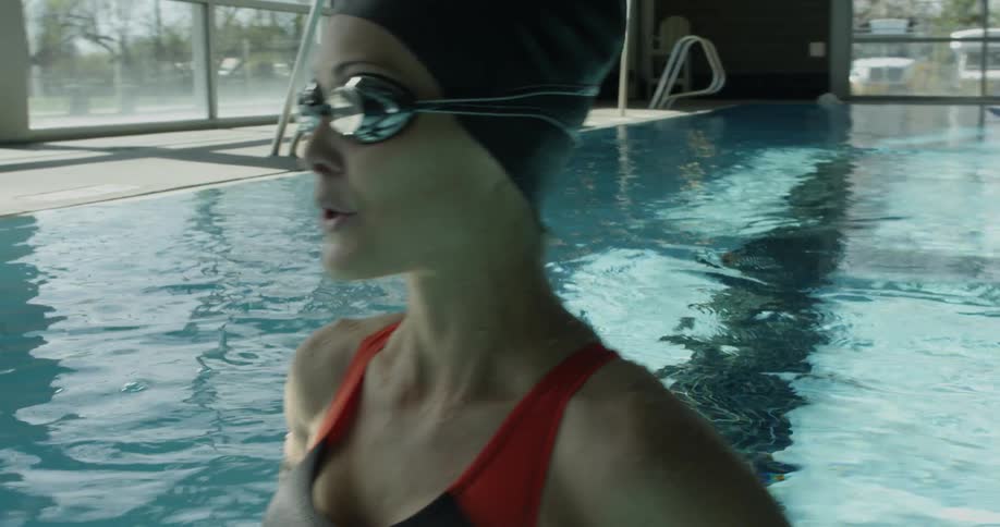 A woman is smiling and breathing deeply as she stands in an indoor swimming pool