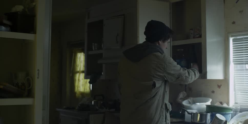 A young man is searching for something in a kitchen cabinet in the morning
