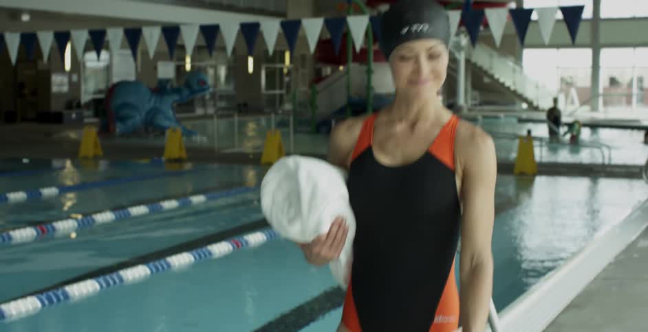 Woman walks next to a swimming pool carrying a towel