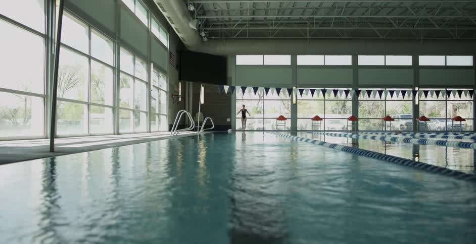 A woman is standing on the edge of a pool and stretching