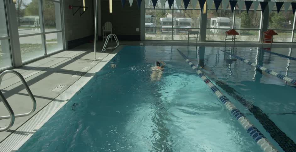 A woman is swimming laps at an indoor pool during the day