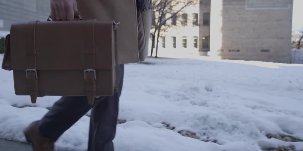 A man walks down a trail by the snow carrying a briefcase