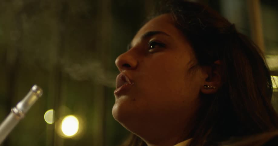 A young woman takes a puff from a hookah