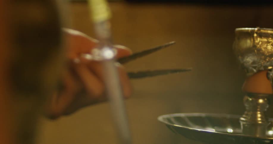A person holds metal tweezers near a sculpture