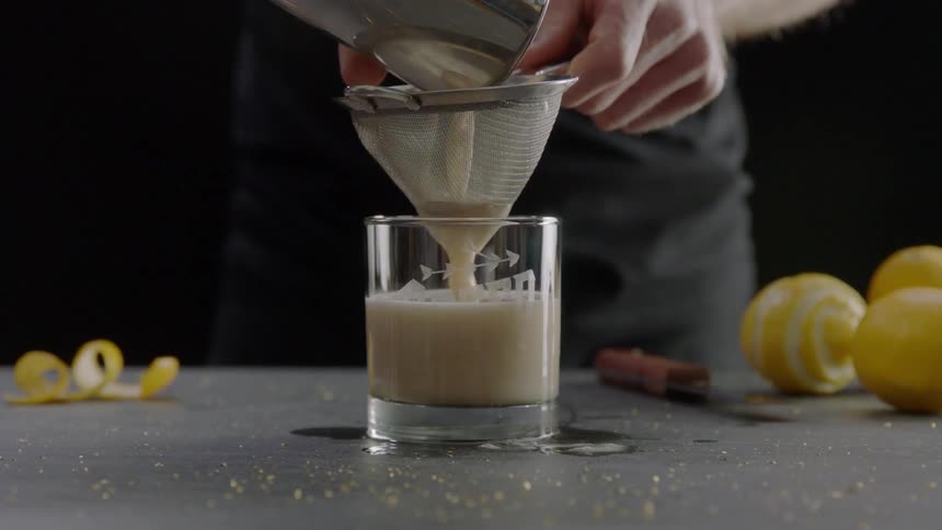 White liquid is poured in a glass through a strainer