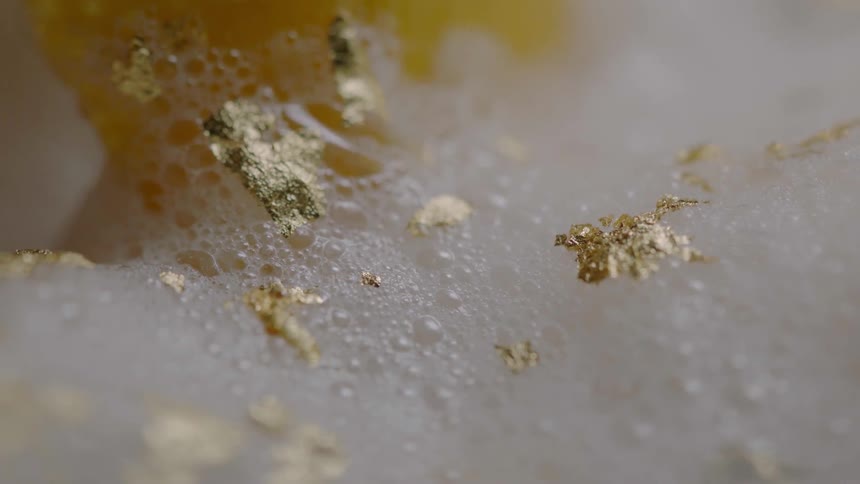 White foam with gold flakes is being stirred by something