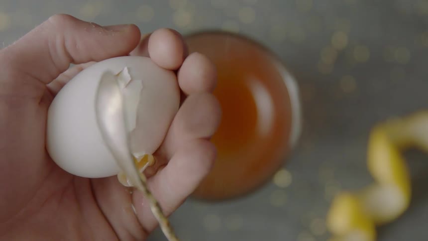 A person cracks an egg with a spoon