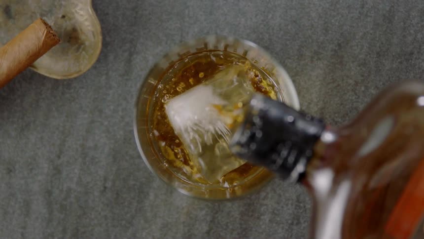 Bourbon is being poured over ice in a glass