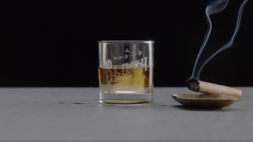 Cigarette burning next to a glass filled with brown liquid