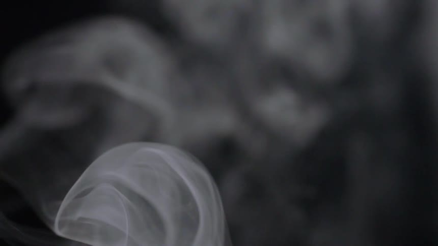 Smoke swirls and rises in a dark room