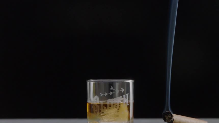 A lit cigar is in an ashtray by a drink