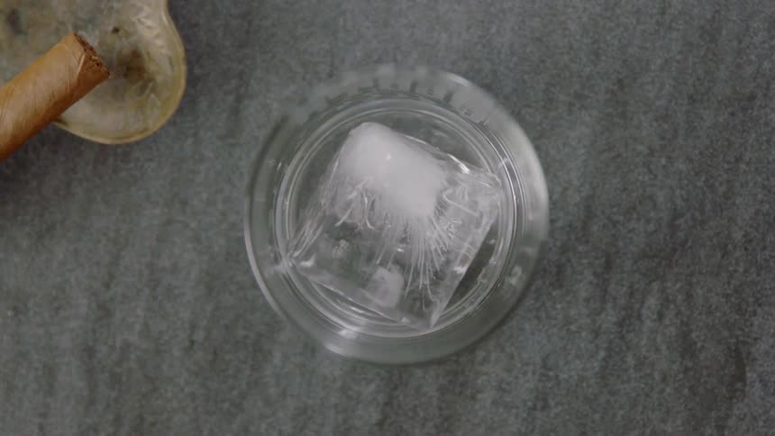 A large square ice cube is tossed into a glass