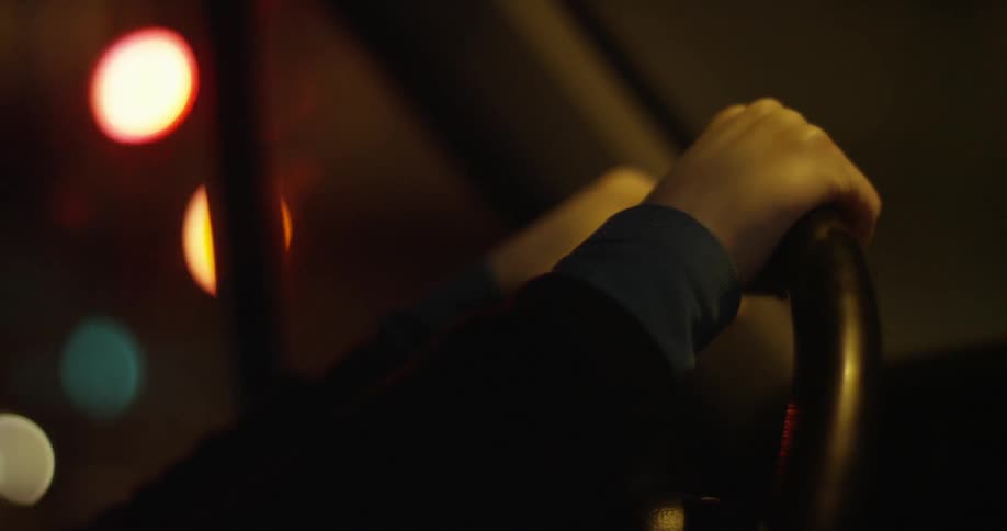 Hands on a car steering wheel driving in a city at night