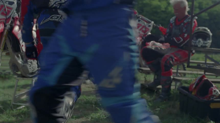 A motocross rider walks to his bike and puts his helmet on