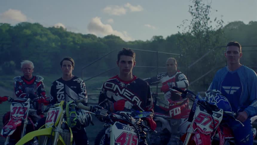 Smoke drifts across a group of motocross riders posing with their bikes