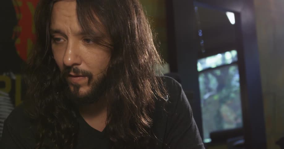 A man with long hair looks down and concentrates