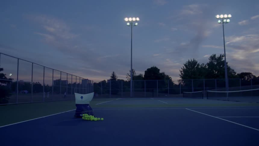 A tennis ball throwing machine is sitting on an empty tennis court