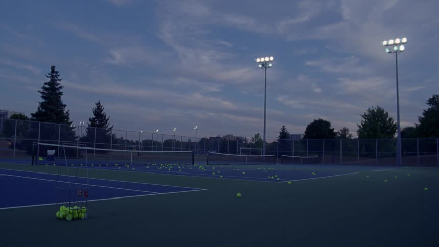 Tennis balls lay around on a blue court under the lights