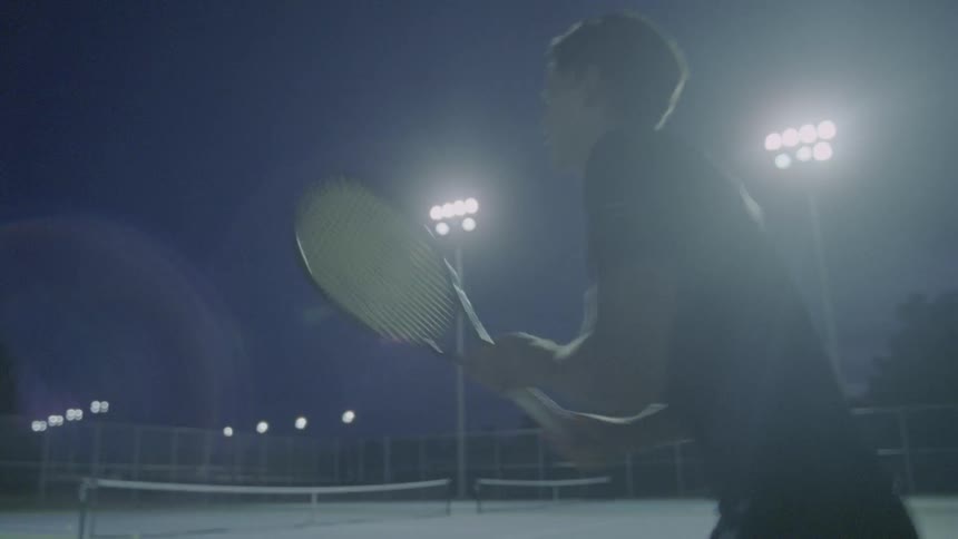 A man is playing tennis on a court at night