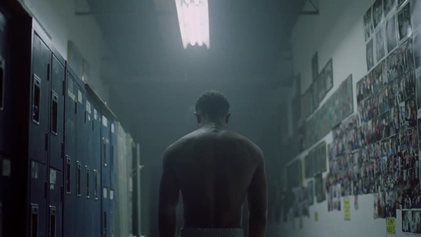 A male athlete standing in a locker room hits a wall with his hand