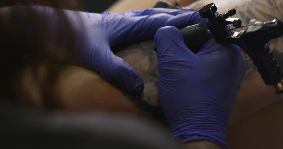 A tattoo artist works on a client