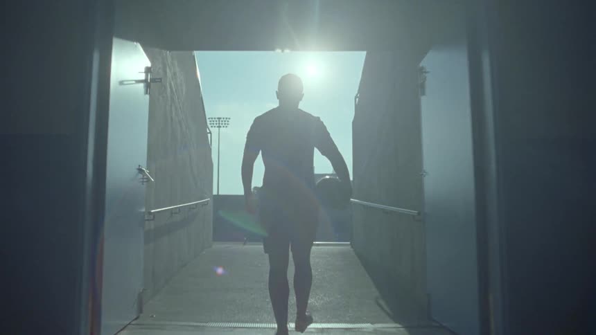A soccer player carries a ball as he walks out of a tunnel into a stadium