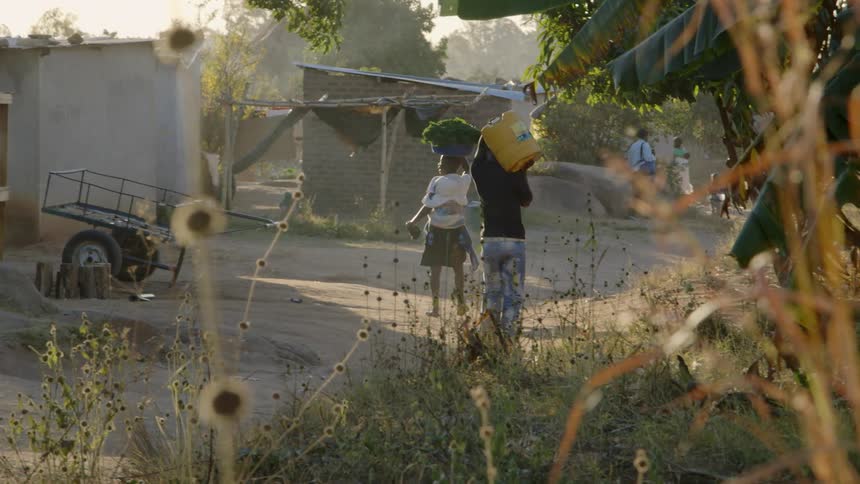 People carry goods along a dusty village road