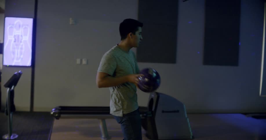 Man dances with a bowling ball and another man and woman dance together in a bowling alley
