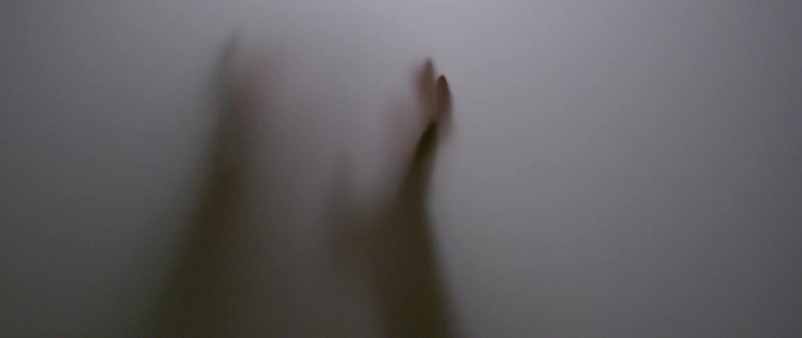 Shadowy figure moves its hands down a frosted surface