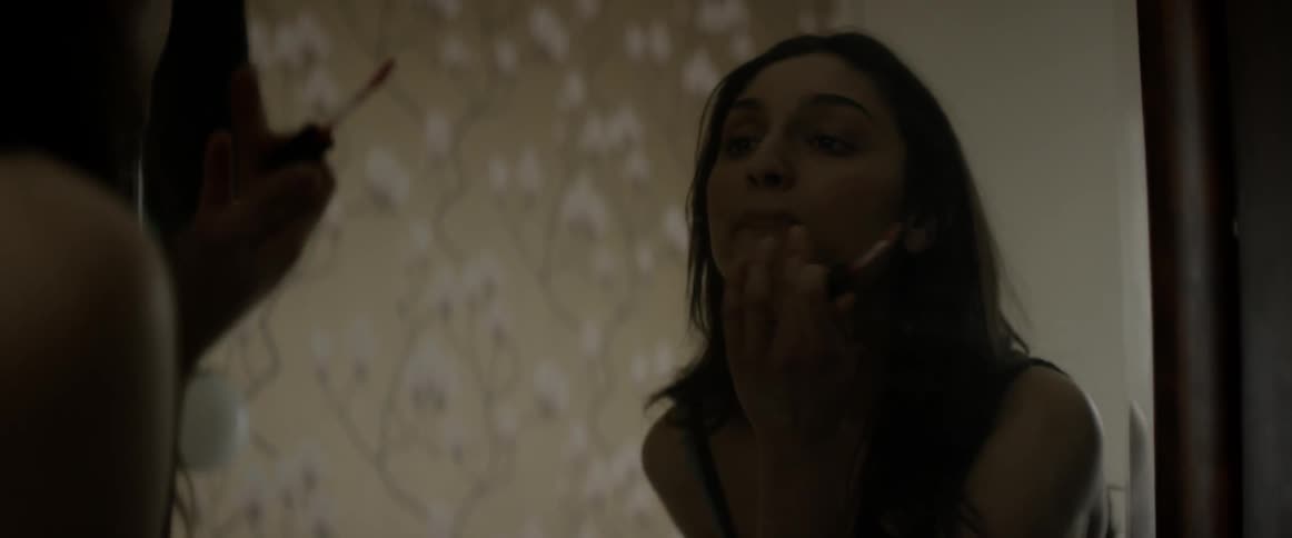 A woman is looking into the mirror and applying makeup