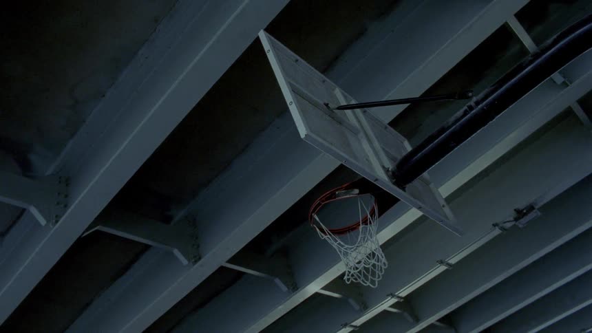 A basketball net hangs from a hoop on a backboard beneath a bridge