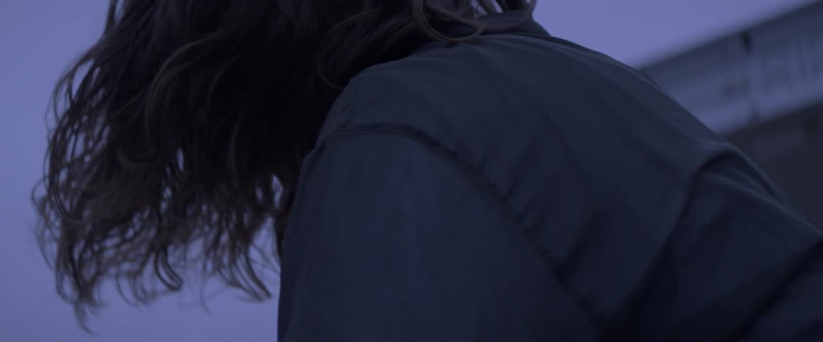 Person with hair covering face sits below a bridge