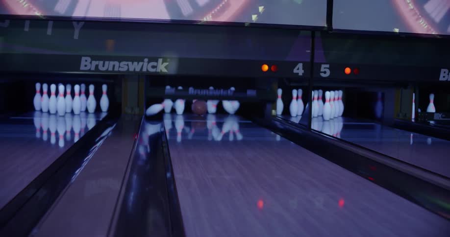 A bowling ball rolls down an alley and crashes into the pins